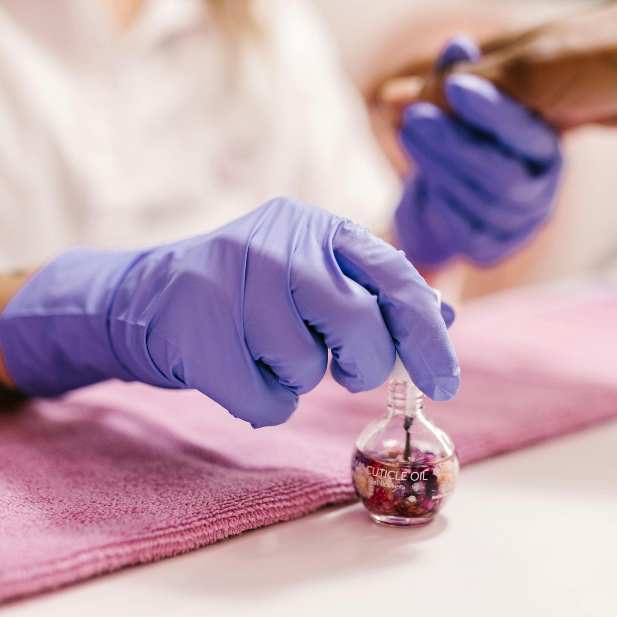 Nail technician applying cuticle oil with dropper bottle, essential nail supply product.
